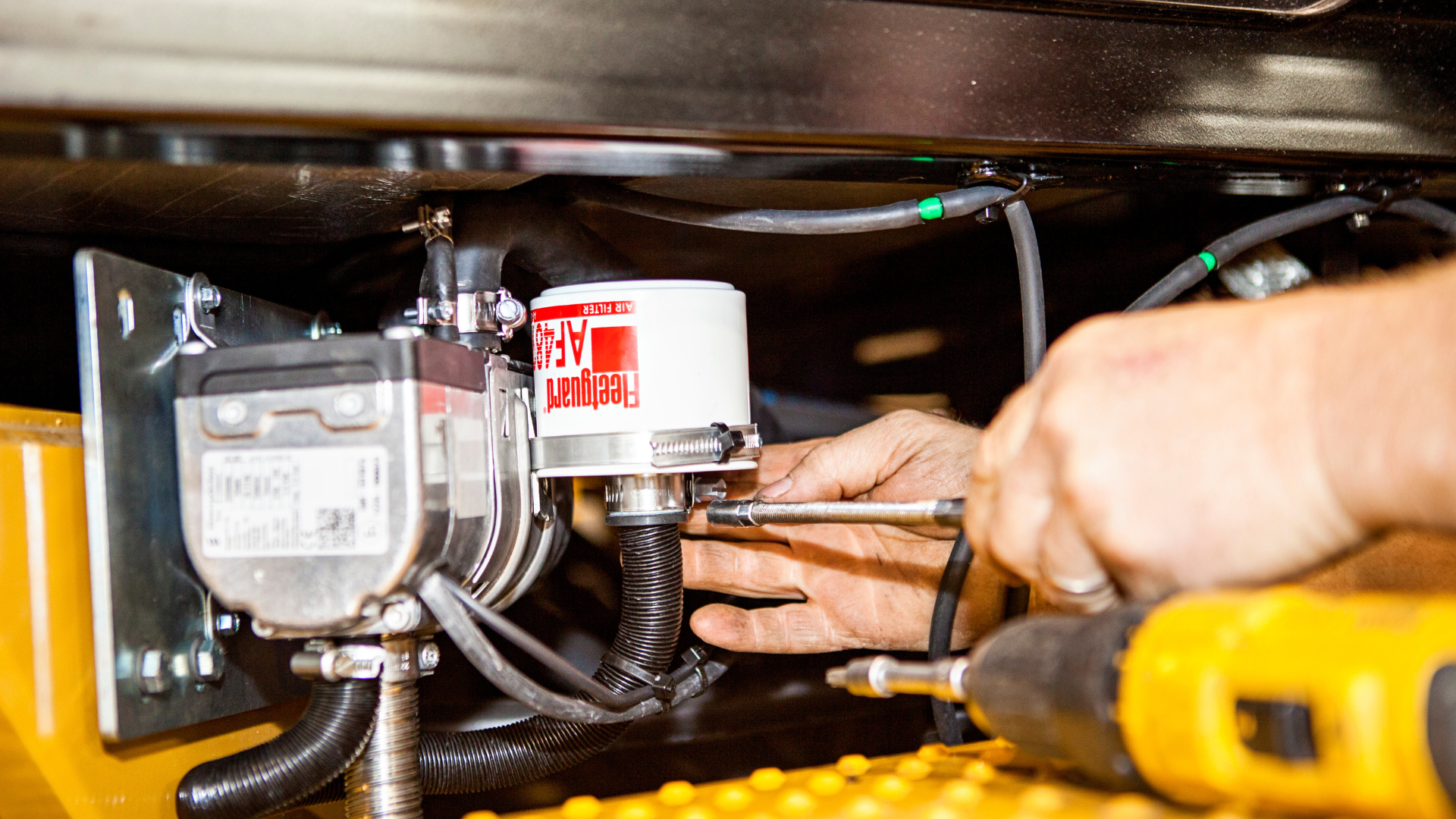 Närbild på STS-tekniker som monterar en smörjpump och filter på entreprenadmaskin med verktyg, fokus på noggrant servicearbete.