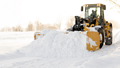 Entreprenadmaskin som plogar snö på vinterväg, illustrerar krävande vinterarbete där fungerande värmare är avgörande.