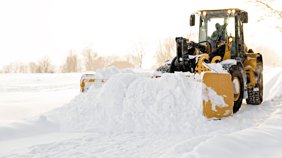 Entreprenadmaskin som plogar snö på vinterväg, illustrerar krävande vinterarbete där fungerande värmare är avgörande.