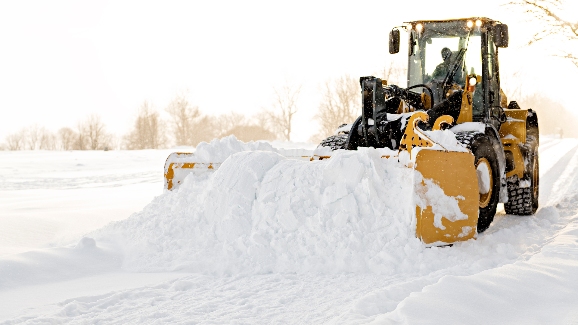 Entreprenadmaskin som plogar snö på vinterväg, illustrerar krävande vinterarbete där fungerande värmare är avgörande.