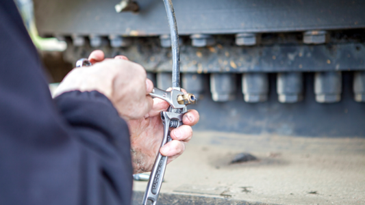 Förare som använder en fettspruta för manuell smörjning av maskinens leder, som kontrast till automatiserad centralsmörjning med centralsmörjsystem.