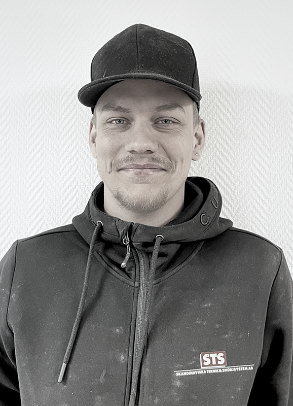 Man wearing a black cap and black hoodie with a small logo on the chest, smiling at the camera.
