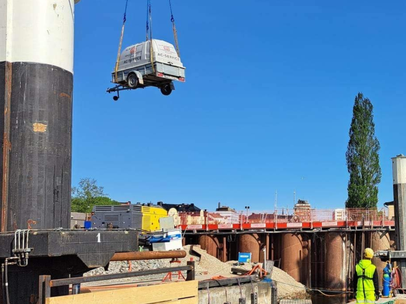 STS mobila AC-service-släp lyfts med kran ut till en pråm vid ett pålningsarbete i hamnmiljö